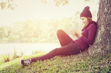 Mobil fon oynarken ağacın altında oturup mutlu güzel kadın