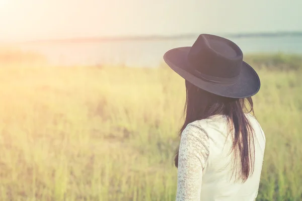 Sad woman wearing black hat standing in a meadow — Stock Photo, Image