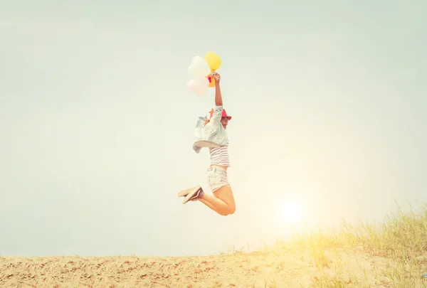Menina bonita pulando com balões na praia — Fotografia de Stock