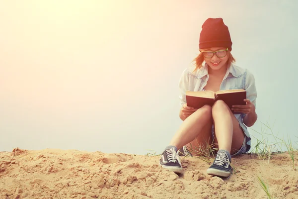 Jong meisje lezen boek en zittend op het strand met sunrise — Stockfoto