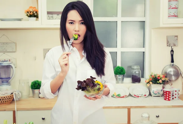 Mooie jonge vrouw die een gezonde salade eten in de keuken — Stockfoto