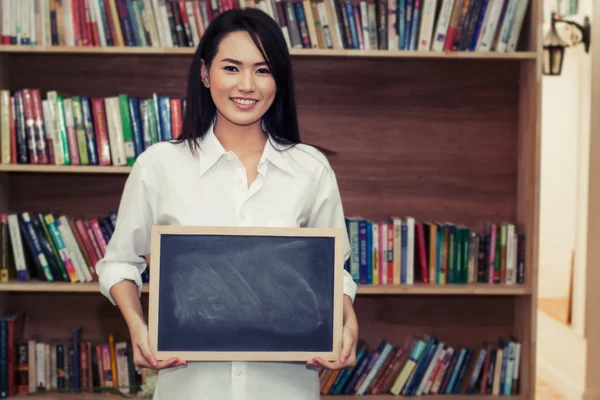 Mooie jonge vrouw die houdt van het bord tegenover bookshe — Stockfoto