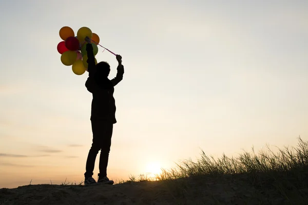 silhouette of Young  woman holding colorful of balloons with sun