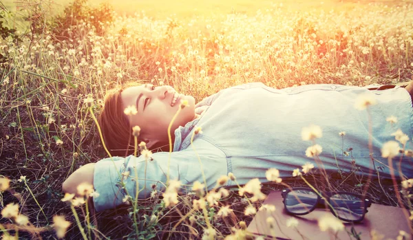 Beautiful young hipster laying down on the dandelion field smile — Stock Photo, Image