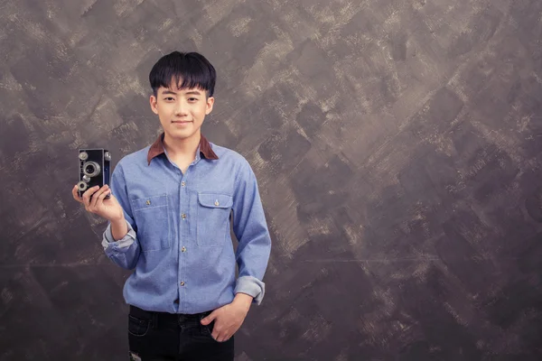 Handsome young man standing holding retro camera on grunge wall — Stock Photo, Image