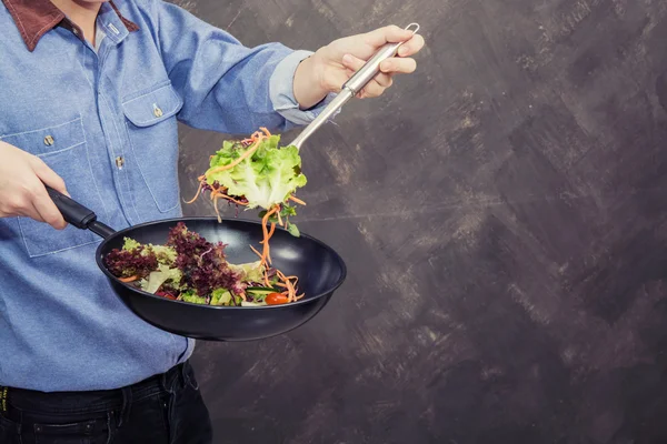 Man cooking salad on the pan on grunge background — Stock Photo, Image