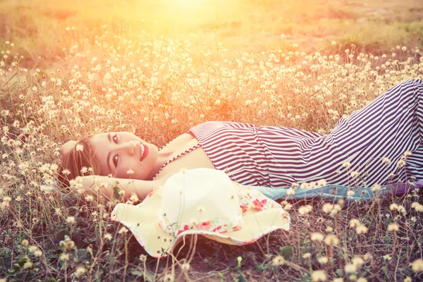 Young sexy woman lying in grass nearing her hat and smiley to ca — Stock Photo, Image