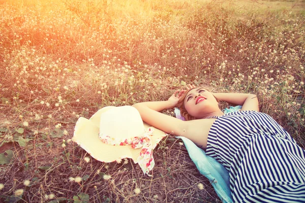 Young sexy woman lying in grass nearing her hat look into the s — Stock Photo, Image
