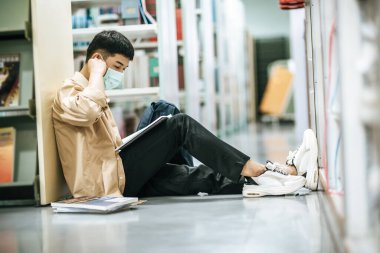 Maskeli bir adam kütüphanede oturmuş kitap okuyor..