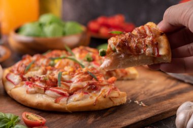 Biber tohumlarıyla dolu tahta bir tabağa yerleştirilmiş pizza. Domates ve sarımsak. Seçici odak.