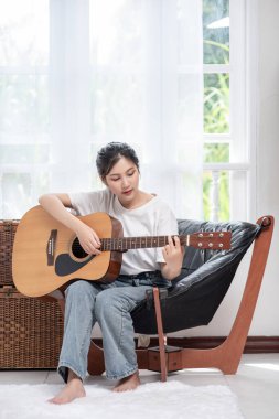 Kız oturuyor ve sandalyede gitar çalıyor..