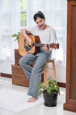 Kız oturuyor ve sandalyede gitar çalıyor..