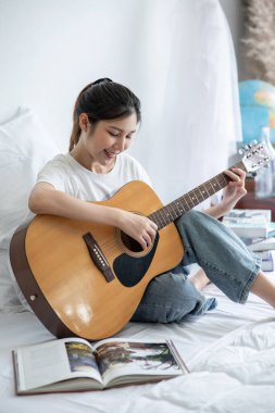 Kız oturdu ve yatakta gitar çaldı..