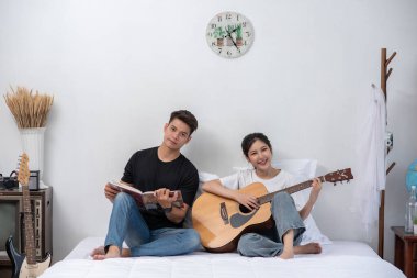 Oturan bir kadın gitar çalıyor ve elinde kitap tutan bir adam şarkı söylüyor..