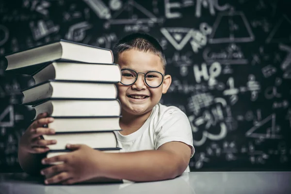 A boy hugging a pile of books in the classroom.