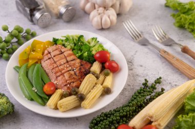 Beyaz susamlı tavuk bifteği, bezelye, domates, brokoli ve beyaz tabakta balkabağı..