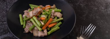 Kızarmış uzun fasulye ve havuç, domuz göbeği ekle, siyah bir tabak koy..