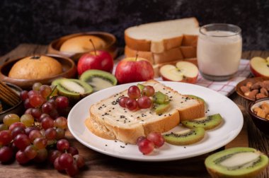 Ekmeği reçelle dağıt ve beyaz bir tabağa kivi ve üzümle yerleştir..