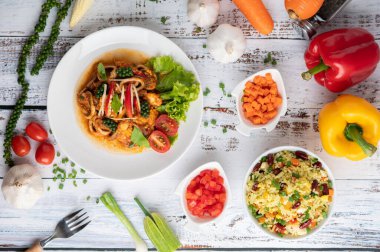 Beyaz tabakta köri ezmesiyle kızartılmış kalamar, sebzeler ve ahşap bir zeminde mezeler. Üst görünüm.