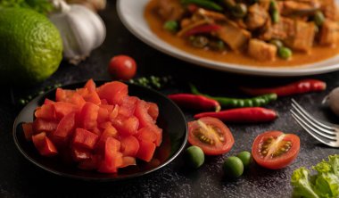 Siyah bir tabakta doğranmış domates ve çimento zemininde kırmızı biber ve limon.