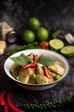 Siyah çimento arka planında baharatları olan beyaz bir kasede yeşil köri.