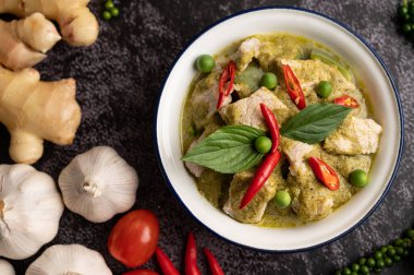 Siyah çimento arka planında baharatları olan beyaz bir kasede yeşil köri.