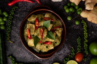 Siyah çimento arka planında baharatlar olan kahverengi bir kasede yeşil köri.