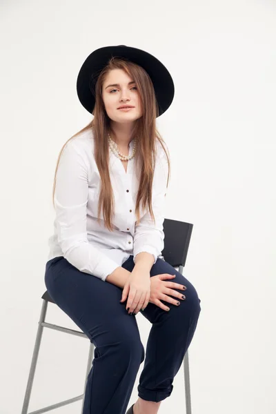 Impresionante modelo femenina sexy atractiva caucásica tímida con pelo morena posando en la mesa en el estudio, vistiendo traje formal y sombrero, aislado sobre fondo blanco —  Fotos de Stock