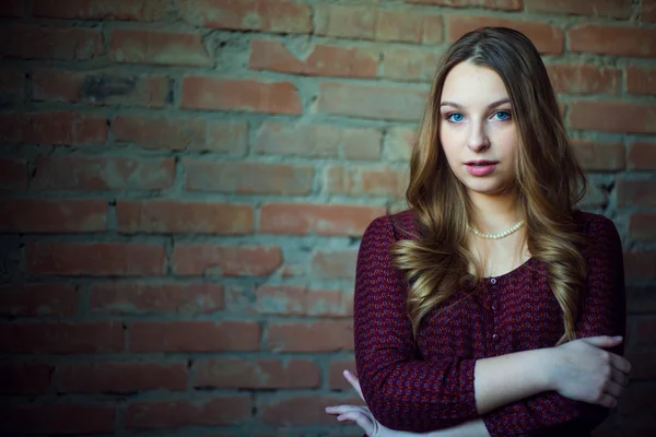 Un giovane modello di moda femminile in abito su uno sfondo muro di mattoni. Sta guardando. . — Foto Stock