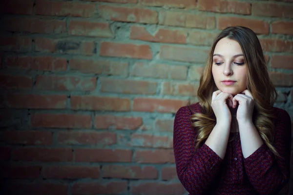 Una joven modelo de moda femenina en vestido sobre un fondo de pared de ladrillo. Ella está mirando . — Foto de Stock