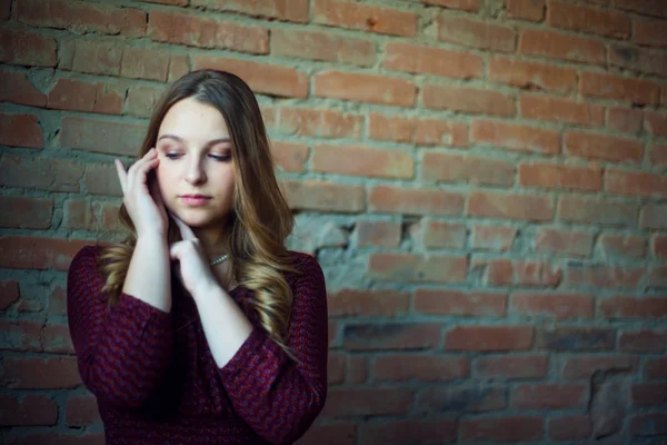 Una joven modelo de moda femenina en vestido sobre un fondo de pared de ladrillo. Ella está mirando . —  Fotos de Stock