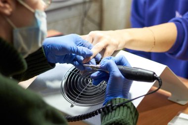 Eldivenli ve maskeli bir manikürcü bir kızın tırnaklarını yapar. Eski tırnakları kesiyorum. Yakın plan.