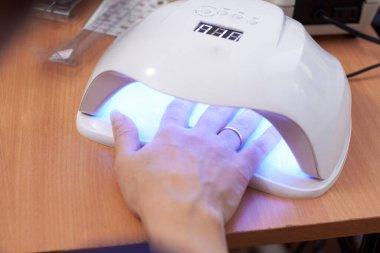 Kız UV lambası ve güzellik salonunda uzun tırnaklarını kurutuyor.