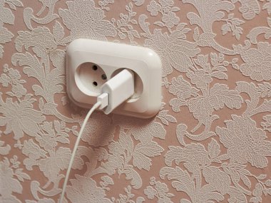 Duvarda beyaz bir elektrik prizi ve telefon şarjı var..