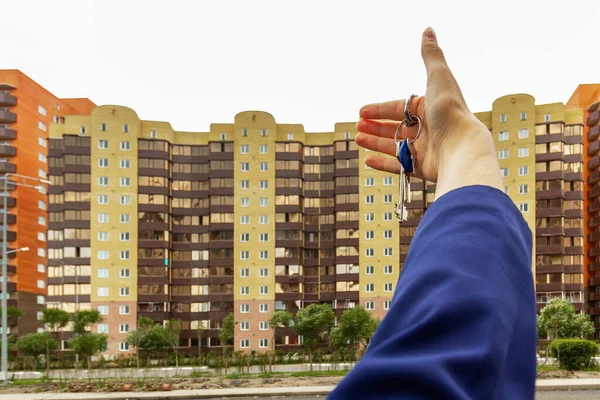 Bir apartmanın arka planında dairenin anahtarlarının olduğu el..