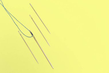 Sarı arka planda mavi iplikli çelik dikiş iğneleri. Dikey dikiş iğneleri ile sarı arkaplan