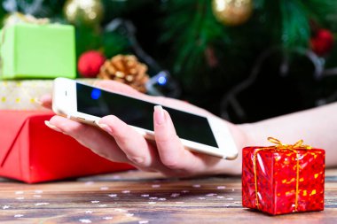 İnsanlar kış tatilinde alışveriş için akıllı telefon kullanıyor. Noel ağacı geçmişi bulanık.