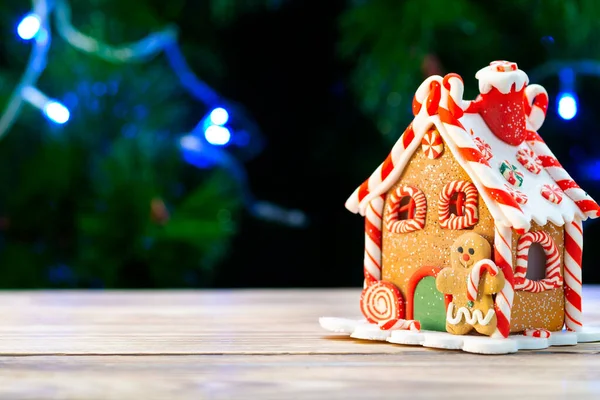 Casa de jengibre sobre una mesa de madera sobre el fondo de un árbol de Navidad —  Fotos de Stock