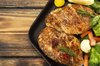 Tavada ızgara tavuk göğsü sebzeler ve otlarla ahşap bir tahtanın üzerinde dilimlenmiş limon.