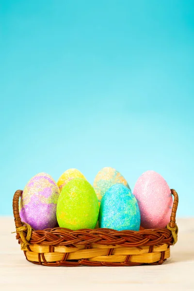 Oeufs de Pâques colorés dans le panier sur la table sur fond bleu — Photo