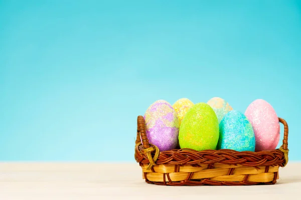 Oeufs de Pâques colorés dans le panier sur la table sur fond bleu — Photo