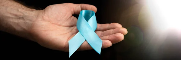 男性的手拿着一条蓝色的带子在深色的背景上 十一月的健康检查 预防前列腺炎 癌症意识 一个月不刮胡子 — 图库照片