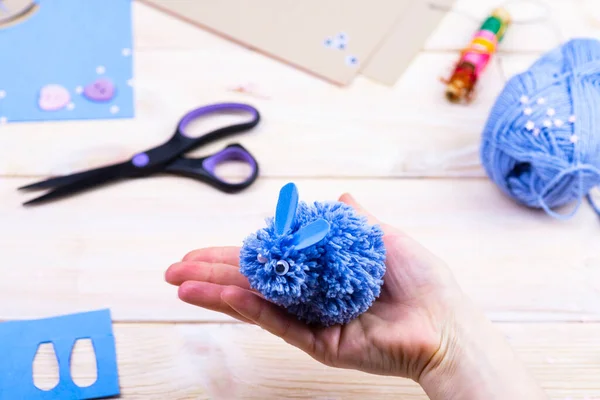 How to make a bunny from pom-poms for Easter decor. Children\'s art project. DIY concept. Hands make a blue Easter bunny out of a pompom. Step by step photo instruction.