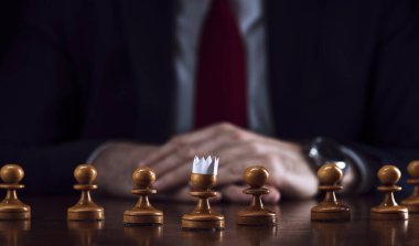 Strateji ve iş planlama kavramı, satranç tahtasındaki bir işadamı, beyaz piyonların önünde dizilmiş, bir tanesi kağıt bir taç, strateji ve taktik, savaşa hazırlık..