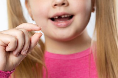 Pembe elbiseli, uzun sarı saçlı, beyaz bir kız süt dişini çekti ve diş temizliği konseptini gülümsetti.