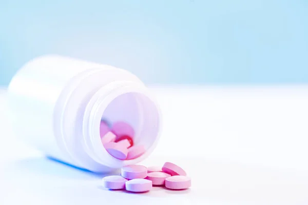 Las píldoras rosadas se vierten de un frasco de plástico de la medicina en una mesa blanca. Industria farmacéutica. Salud y medicina. Concepto farmacéutico. Interacciones medicamentosas — Foto de Stock