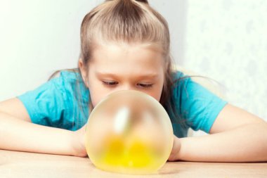 Sarışın bir çocuk balon şişiriyor. Bir balçık oyuncağı oyna. Evde balçık yapıyorum..