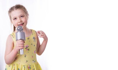 Sarışın küçük bir kız elinde mikrofona şarkı söylüyor. Güzel bir çocuk samimi mutluluk ve pozitif duygularını gösterir. Örgülü saçlar ve sarı bir elbise..