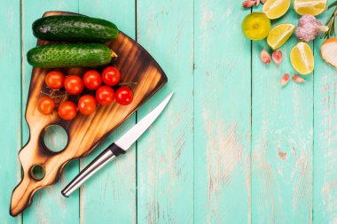 Eski ahşap bir masanın tahta kesme tahtası. El yapımı doğrama tahtası. Taze domates, salatalık, limon dilimleri, baharatlar ve bir kesim tahtası. Metin için yeri olan üst görünüm.