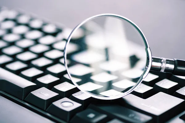 Magnifying glass on the keys of a black computer keyboard.